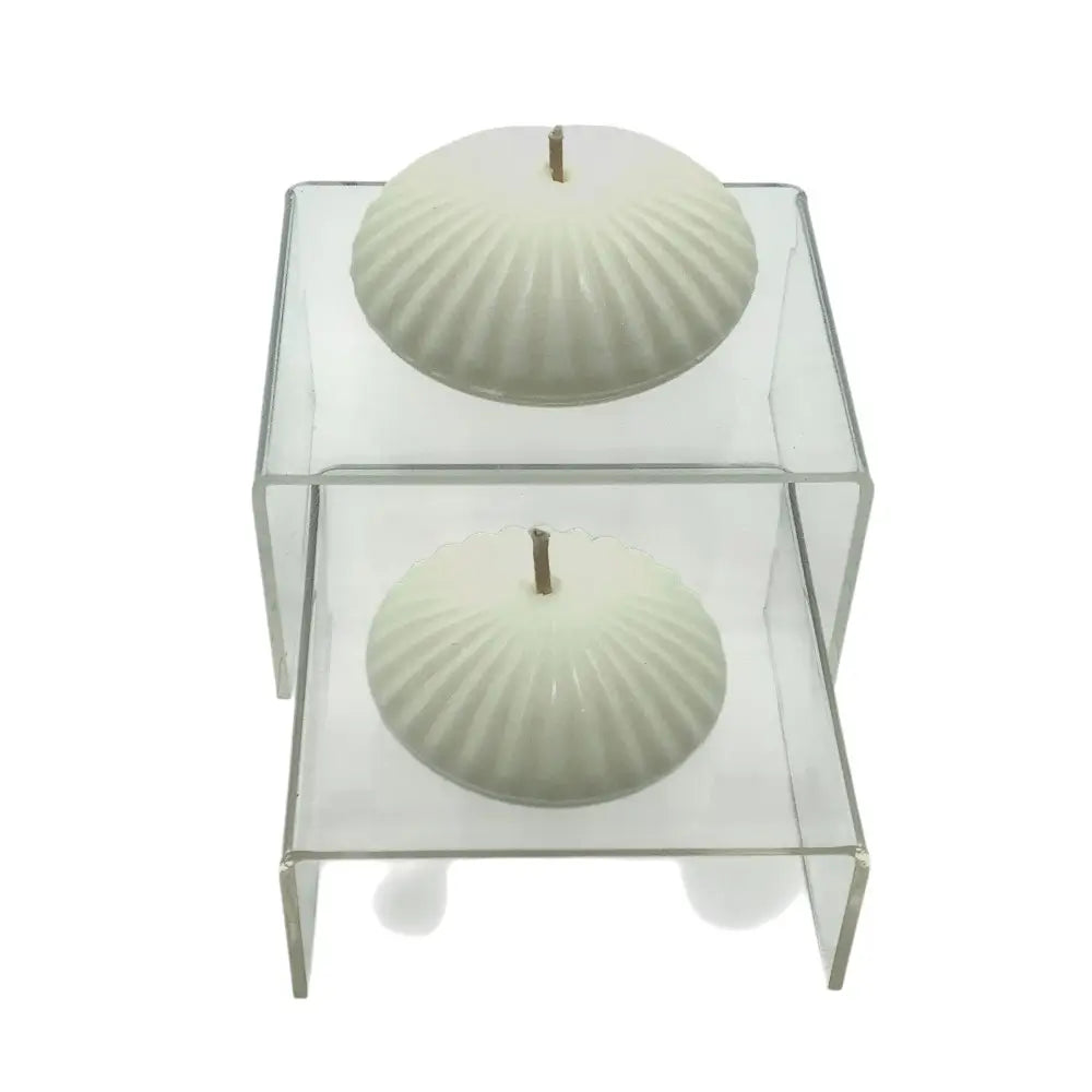 Two white floating candles on display upon glass podiums