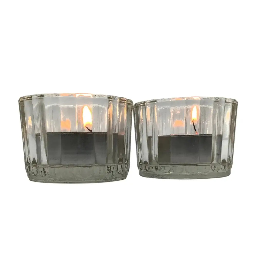 Two clear glass candle holders with lit candles on a white background