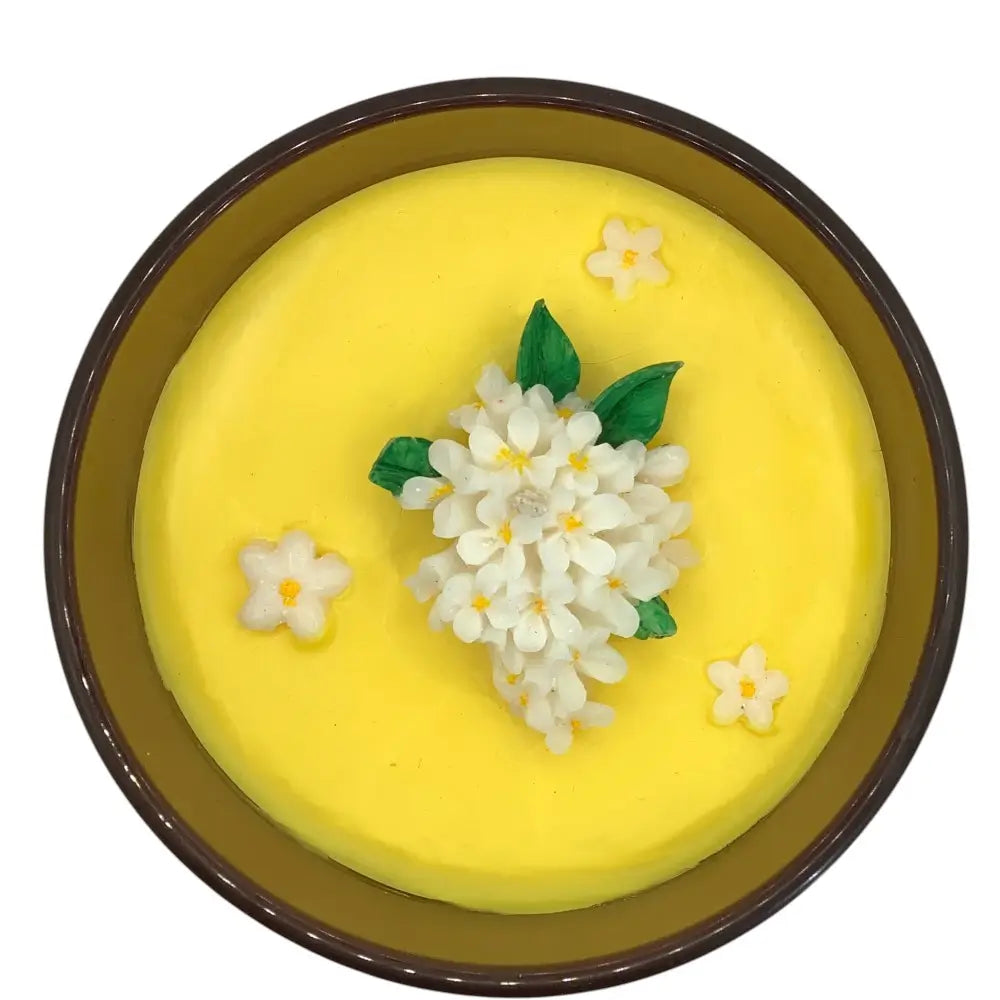 Yellow candle top with floral decorations in a brown jar on a white background