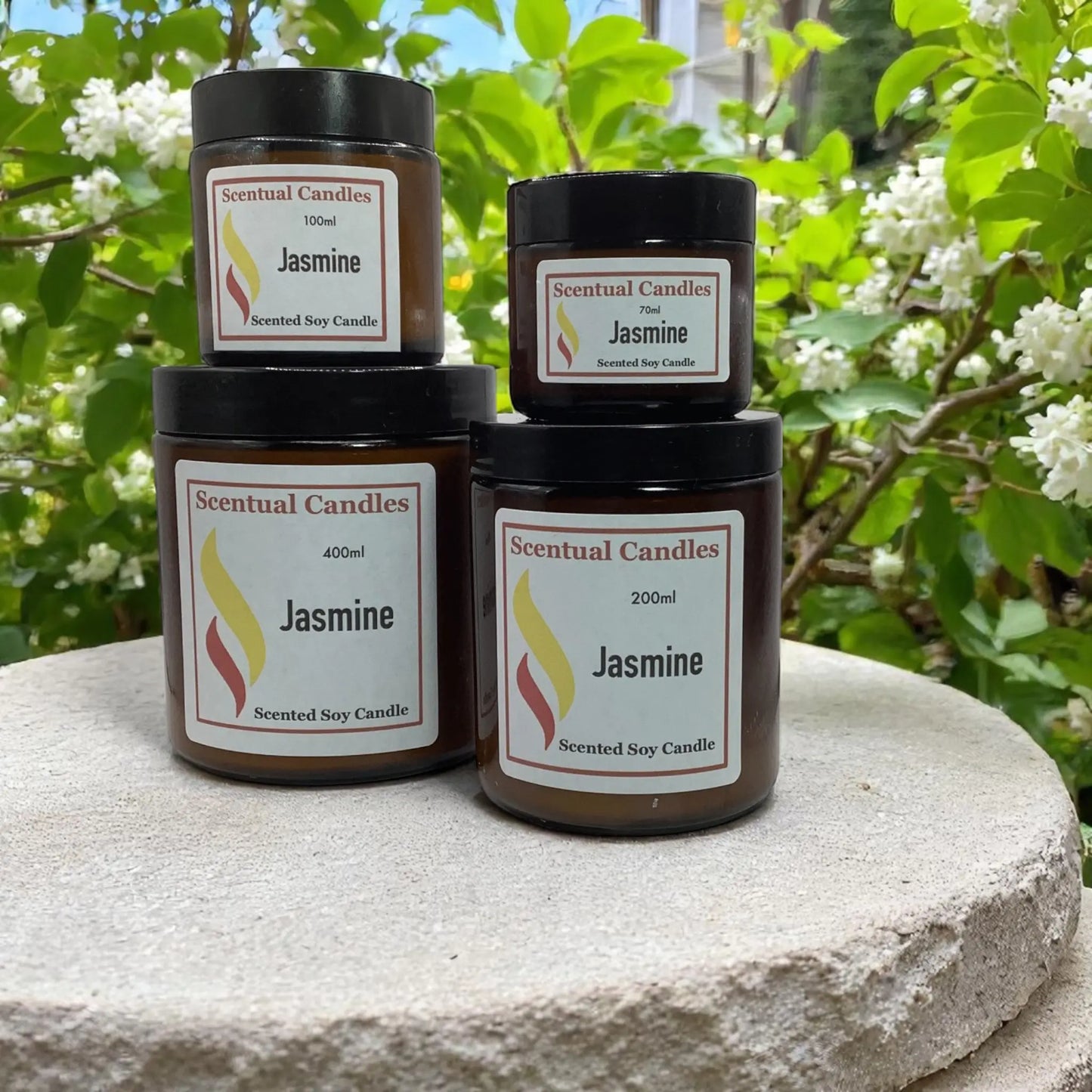 Jasmine Scented Soy Candle Sizes upon a stone pillar in a garden with jasmine
