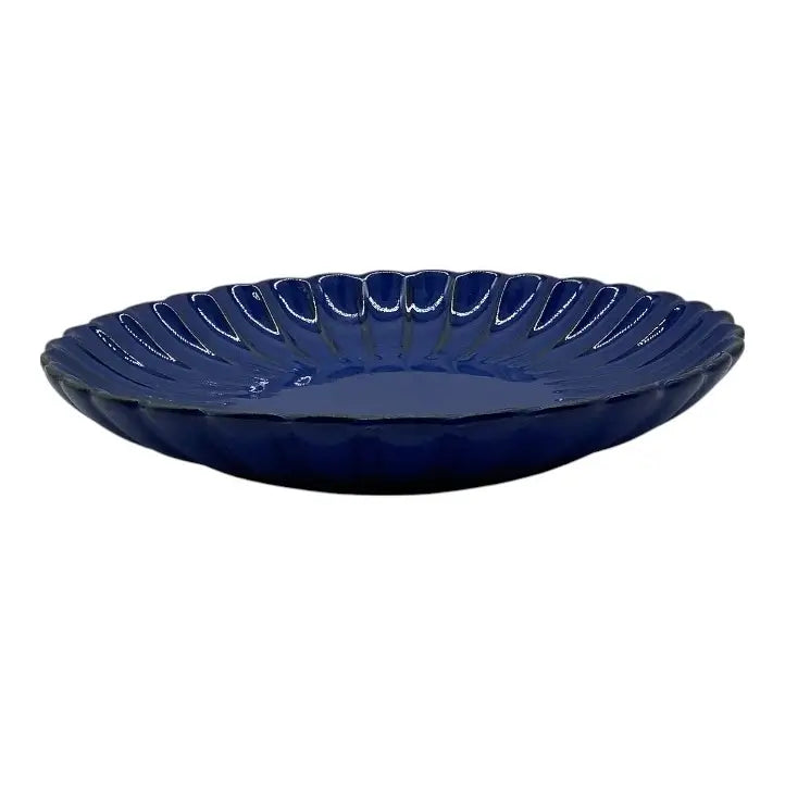 Blue ceramic candle holder plate with scalloped edge on a white background