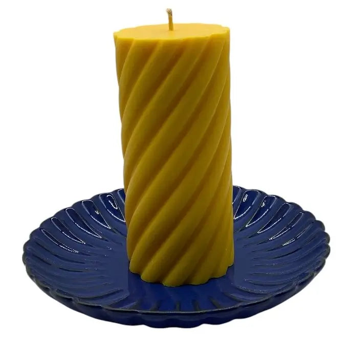 Yellow spiral candle on a blue decorative ceramic candle holder against a white background
