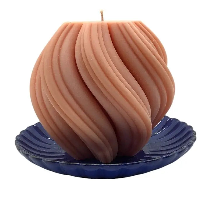 Beige candle with wavy design on a blue ceramic candle holder against a white background