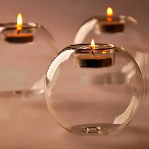 Clear glass candle holders with lit candles on a reflective surface