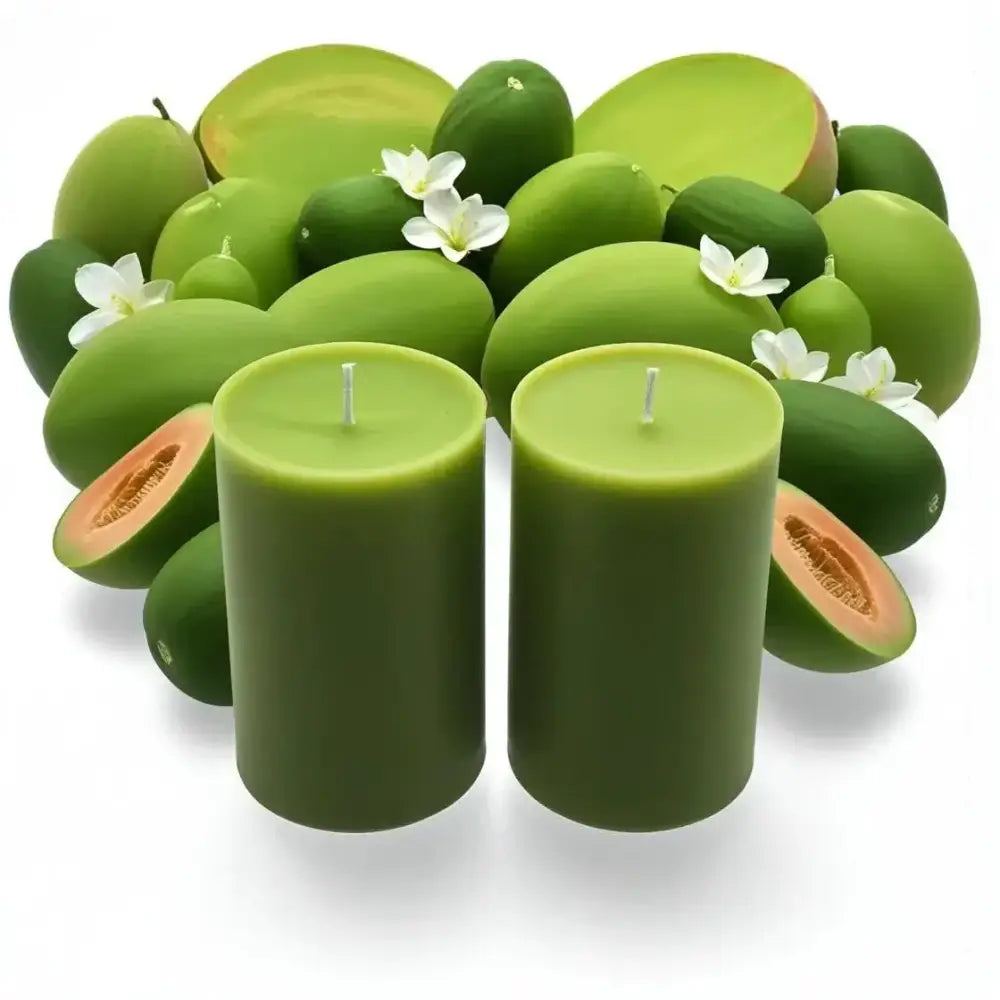 Set of two green fruit scented soy candle set surrounded by fresh melons and flowers.