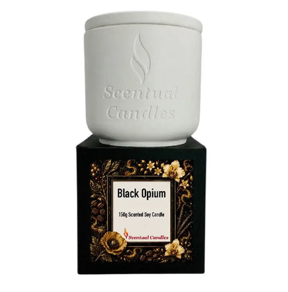 Black Opium Candle in a white ceramic jar on a decorative black box with floral design.