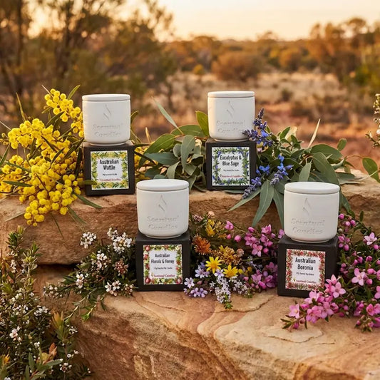 Australian Botanicals scented candle set. Four candles on a rock with Australian native flowers in the foreground and a natural landscape in the background.