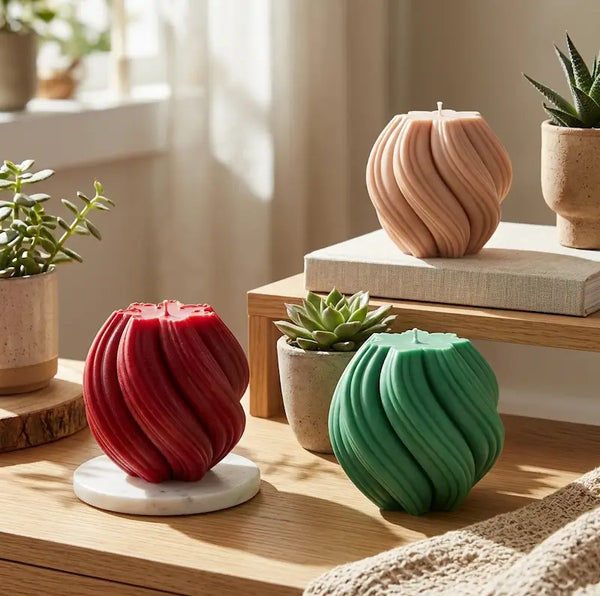 Three vibrant Ball Candles in red, green, and peach colors displayed on a wooden table with potted plants.