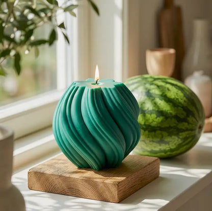 Extra large Ball Candle in teal color on wooden base with a lit wick, inspired by sculptural design.