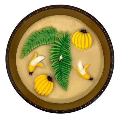 Decorative scented candles top with banana and leaf designs on a beige surface, set against a white background.