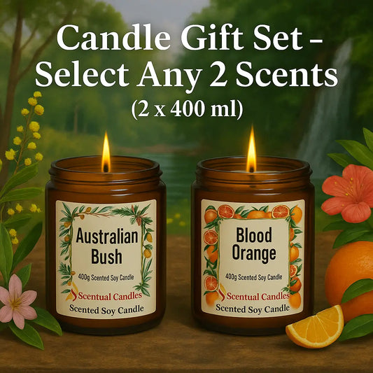 Two lit candles with labels 'Australian Bush' and 'Blood Orange' on a natural background with flowers and fruits.