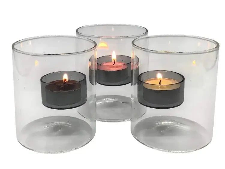 Set of three clear glass candle holders with lit tealight candles inside on a white background