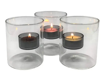 Set of three clear glass candle holders with lit tealight candles inside on a white background