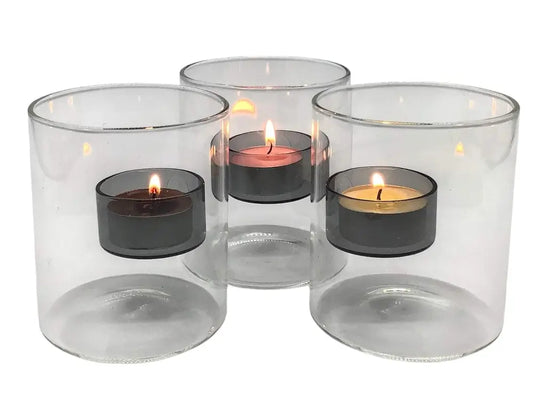 Set of four clear glass candle holders with lit tealight candles inside on a white background