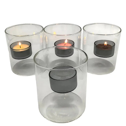 Four clear glass candle holders with small candles inside on a white background