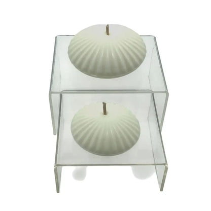 Two white floating candles on display upon glass podiums