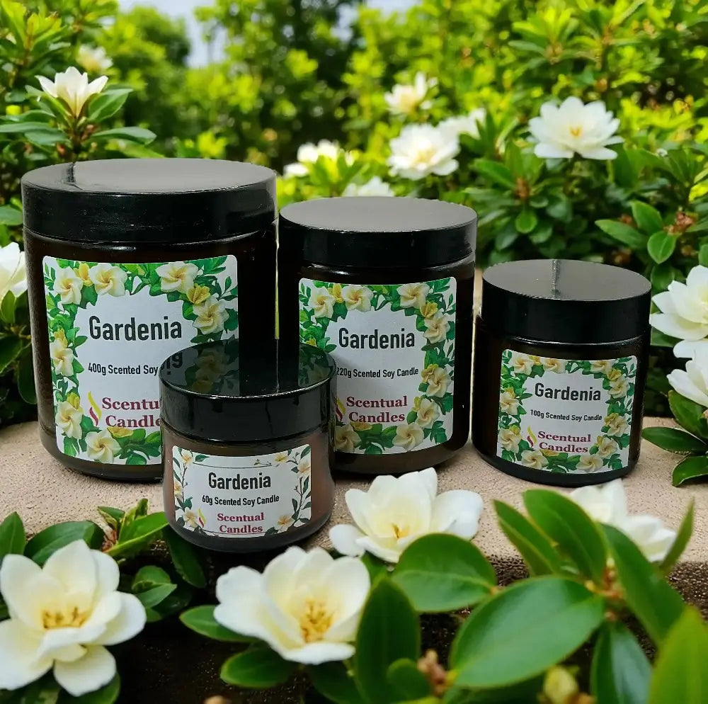 Four black candles labeled 'Gardenia' with floral designs on a natural surface surrounded by gardenia flowers.