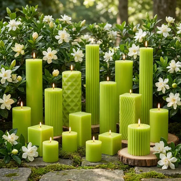 gardenia scented green candles of various shapes and sizes on a stone surface with white flowers in the background.