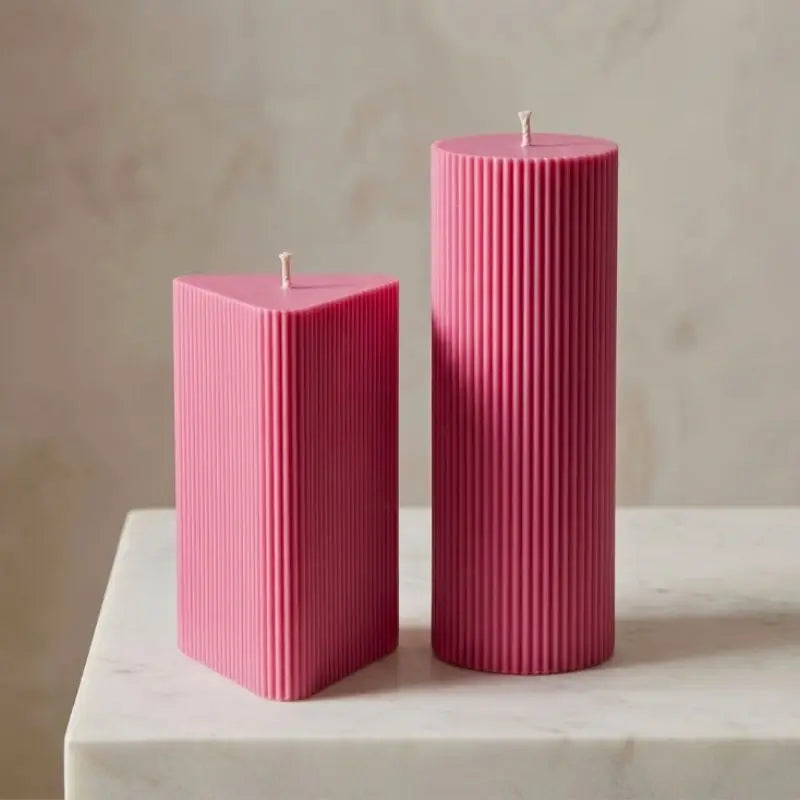 Geometric Pillar Candle set featuring a pink ribbed triangle and tall column on a marble surface.