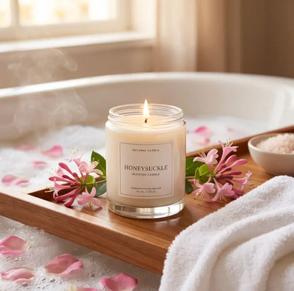 Honeysuckle scented candle on a wooden tray with flowers and bath salts in a bathtub.