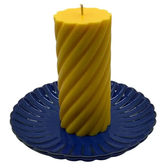 Yellow spiral candle on a blue decorative ceramic candle holder against a white background