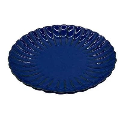 Blue ceramic candle holder plate with decorative edge on a white background