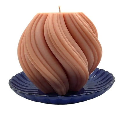Beige candle with wavy design on a blue ceramic candle holder against a white background