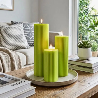 Ribbed Candles - Set of 3 Pillars in vibrant green, displayed on a wooden table with a cozy living room background.