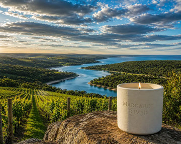 Margaret River Candle on a rocky surface with vineyards and a scenic river view in the background.