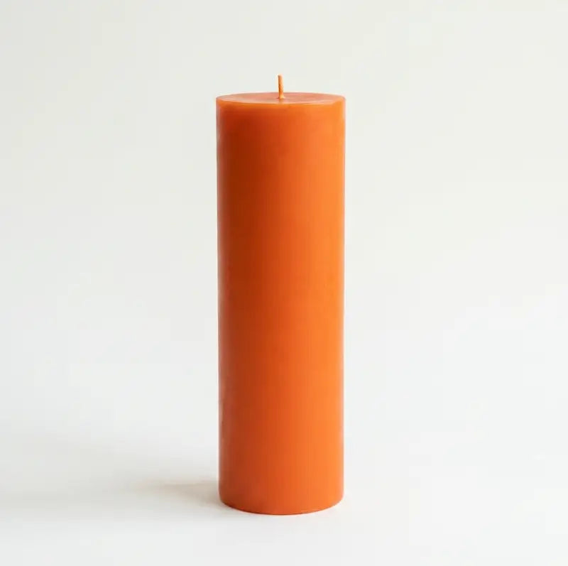 Big Candle in vibrant orange color standing tall on a simple background, perfect for adding bold décor.
