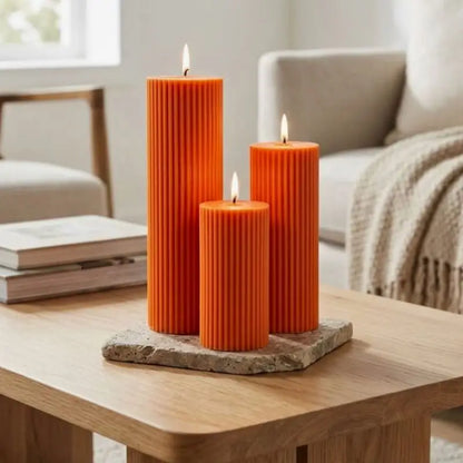 Ribbed Candles - Set of 3 Pillars in orange, displayed on a wooden table with a natural stone base.